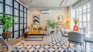 A modern living room with a sofa, coffee table, and chairs. There are potted plants, a round mirror, and a dining table with chairs. The room has large windows and a geometric patterned floor. - w* | Extraordinary 2BR in Plaza Herrera (Panamá)