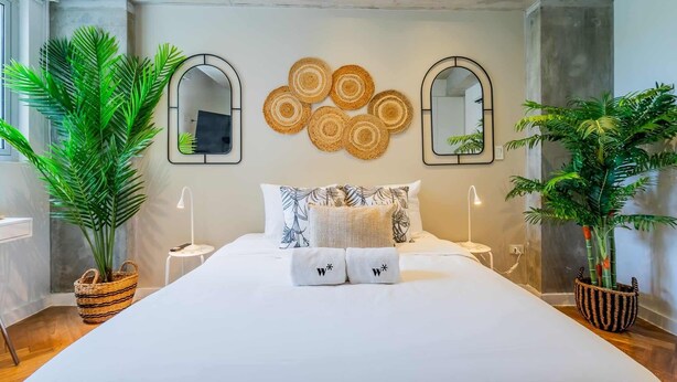 A modern bedroom with a large bed, two bedside tables, a wall-mounted mirror, and decorative woven baskets. - w* | Extraordinary 2BR in Plaza Herrera (Panamá)