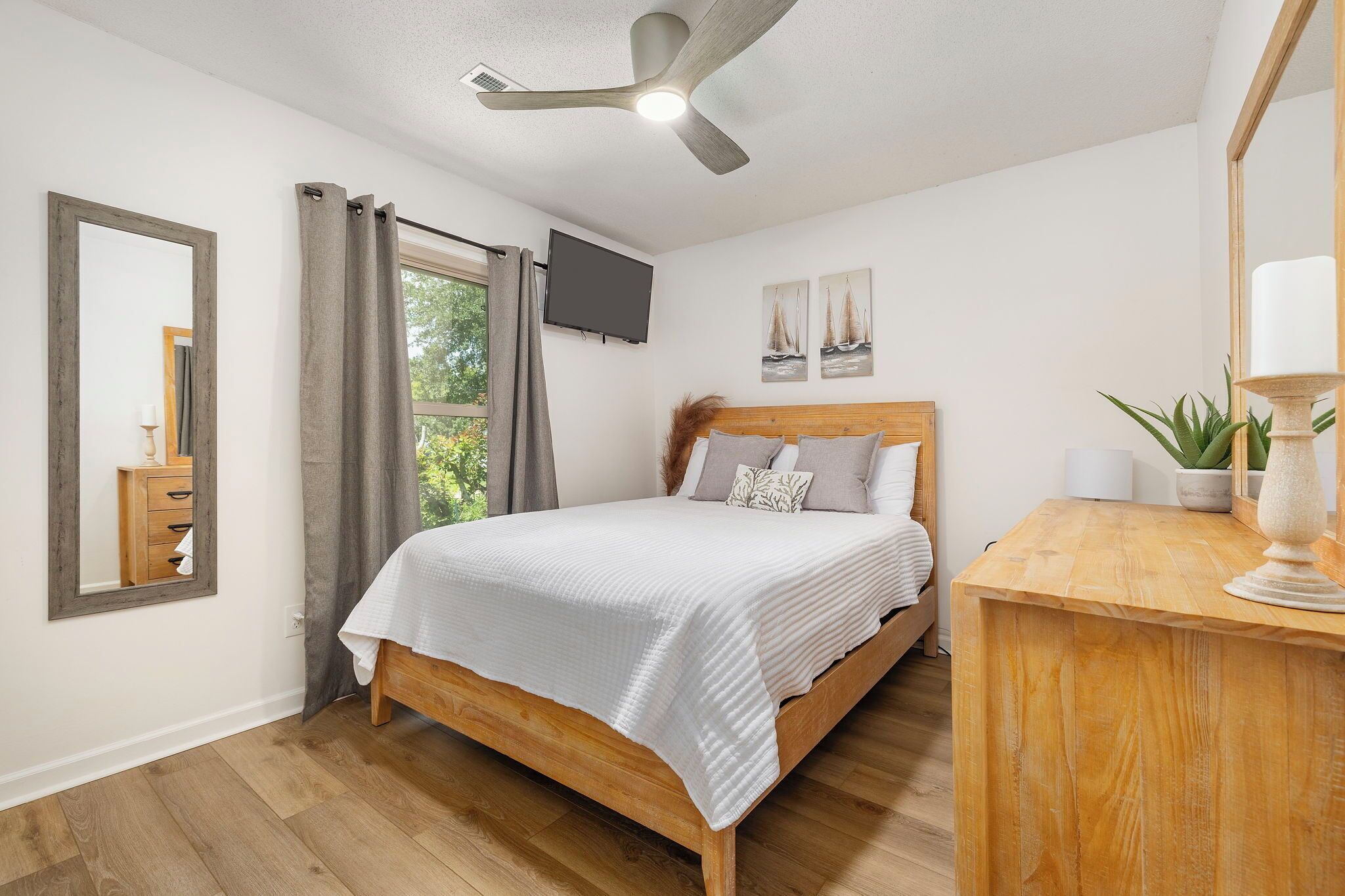 Une chambre à coucher avec un lit en bois, un ventilateur de plafond, une télévision et une fenêtre avec des rideaux.
