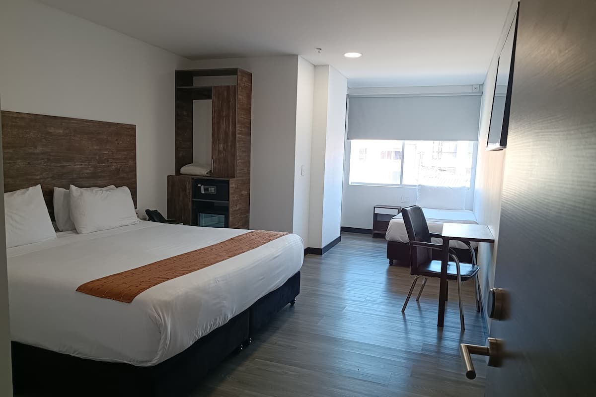 A hotel room with a large bed, a desk, a chair, a wardrobe, and a window with a view of the outside.