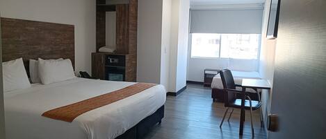 Habitación de hotel con una cama grande, un escritorio, una silla, un armario y una ventana con vistas al exterior.