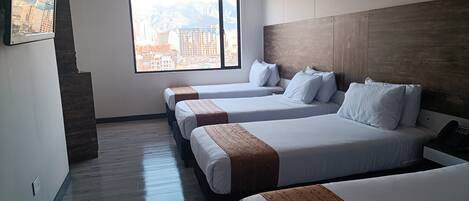 Habitación de hotel con tres camas, un ventanal y vistas a la ciudad, y una pared decorativa de madera.