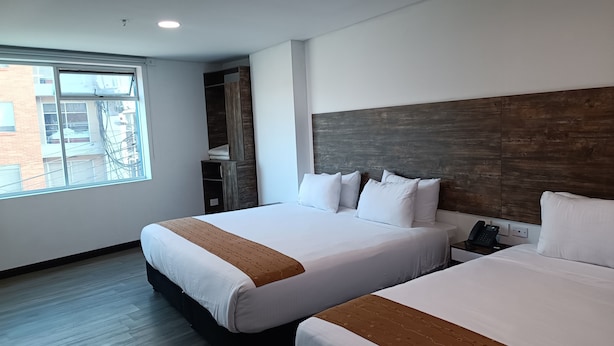 A hotel room with two beds, a wooden headboard, a window with a view of buildings, and a telephone on the nightstand. - HOTEL AMERICAN VISA CORPORATE (Bogotá)