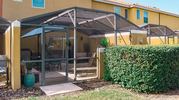 Un patio cubierto con puertas de vidrio, una zona de estar con sillas y una mesa, y un seto bien cuidado.