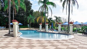 Zona de piscina con suelo a cuadros, sillas de descanso y sombrillas.