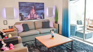 Una sala de estar con un sofá, una mesa de centro y una figurita de Mickey Mouse. En la pared, un cuadro grande de un castillo.