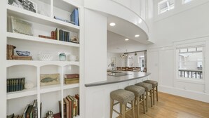 A spacious kitchen with white cabinetry, a bar area with stools, and a view through a window. - Designer Home in SeasideFL, 272 feet to beach, + 2 Bikes! (Santa Rosa Beach Fl)