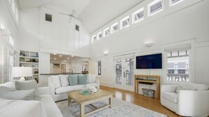 A spacious living room with a high ceiling, white walls, a wooden coffee table, and a large flat-screen TV. - Designer Home in SeasideFL, 272 feet to beach, + 2 Bikes! (Santa Rosa Beach Fl)