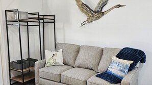 Un salon avec un canapé gris, une décoration murale, une étagère en métal noir et un plancher en bois.