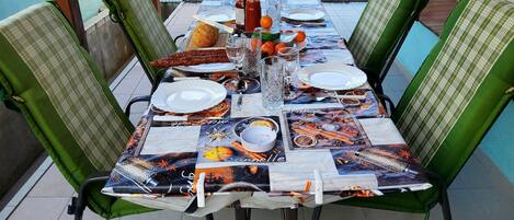 Una mesa de comedor dispuesta con platos, cubiertos y una botella de agua, rodeada de sillas verdes.