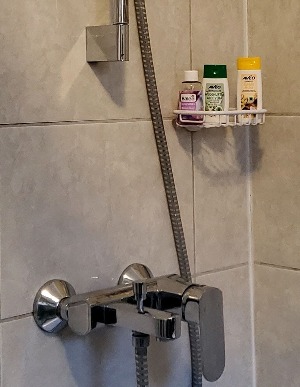 A shower with a chrome faucet and a handheld showerhead, a towel rack with toiletries, and a towel rack with a mirror.