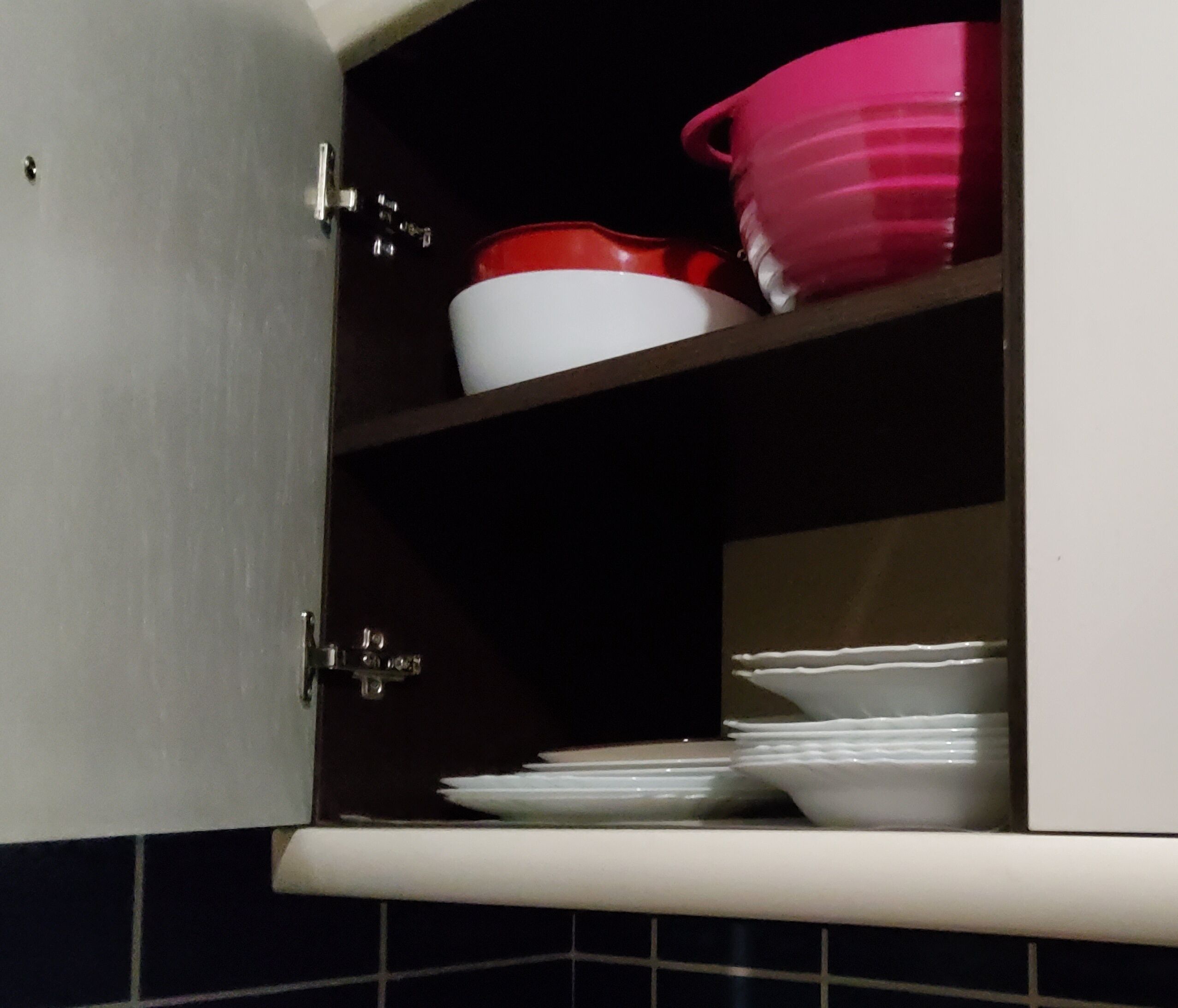 A kitchen cabinet with a white interior and a tiled backsplash.