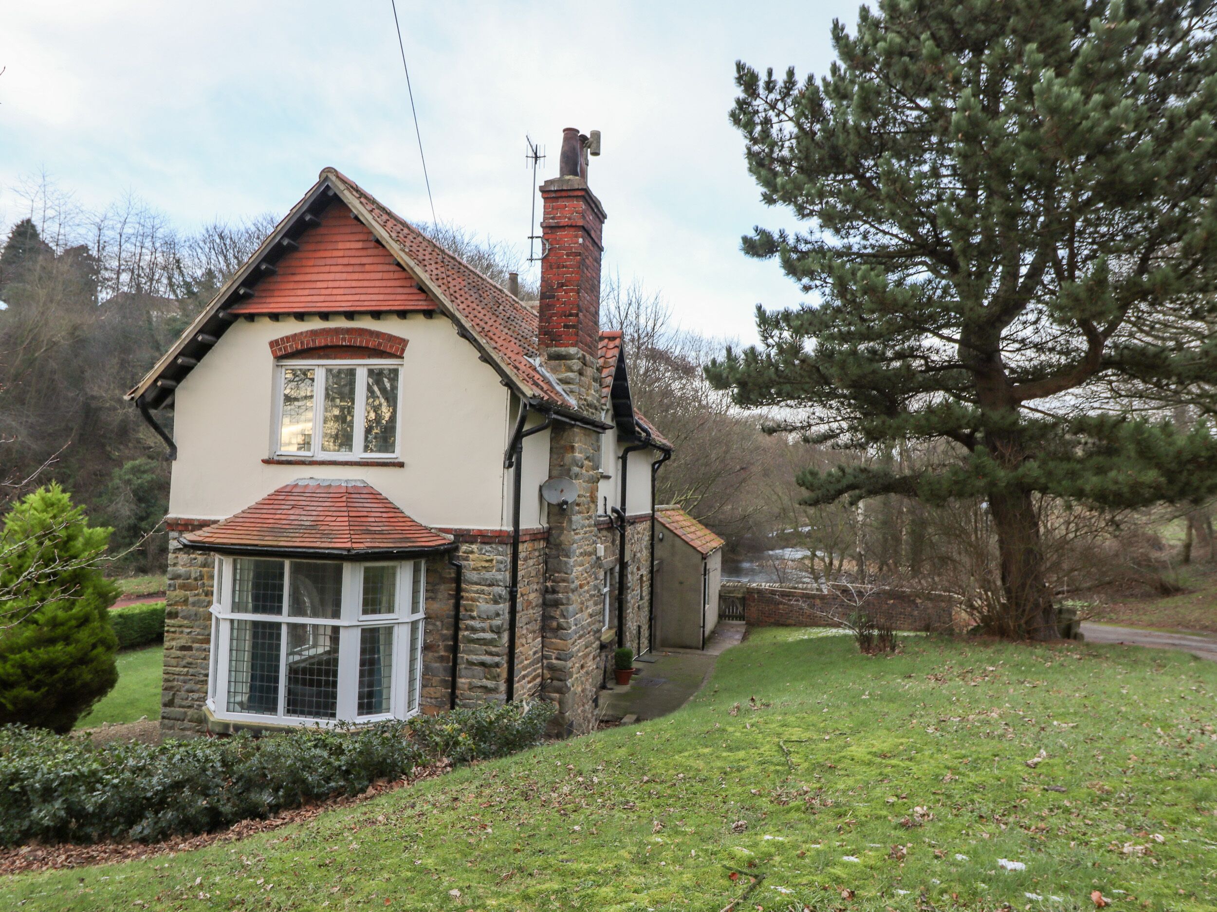 A two-story house with a red-tiled roof, stone walls, and a large window.
