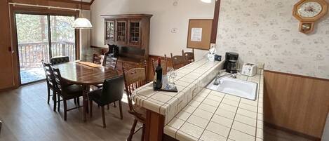 A dining area with a wooden table and chairs, a kitchen with a tiled countertop and sink, and a wooden cabinet.