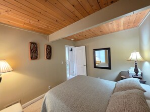 A bedroom with a wooden ceiling, a bed with patterned bedding, a nightstand with a lamp, and two wall-mounted decorative items. - Park View Paradise 3 Bedroom Condo by RedAwning (Tahoe City)