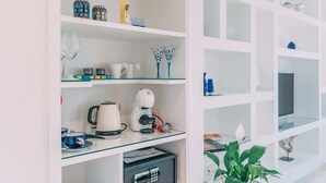Une cuisine bien aménagée, équipée d’une machine à café, d’un service à thé et de divers articles en verre, le tout rangé sur des étagères.