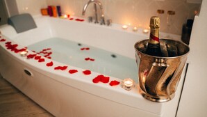 Une baignoire remplie de pétales de rose et une bouteille de champagne dans un seau en métal.