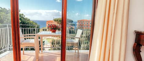 A balcony with a table and chairs, overlooking a scenic view of the sea and buildings.