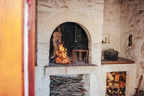 Une cheminée en pierre avec un feu qui crépite à l’intérieur, une petite table et un pot posé sur le manteau de la cheminée.