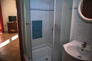A bathroom with a glass shower enclosure, a sink, and a tiled wall.