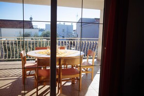 A balcony with a round table and chairs, a view of buildings, and a tiled floor.
