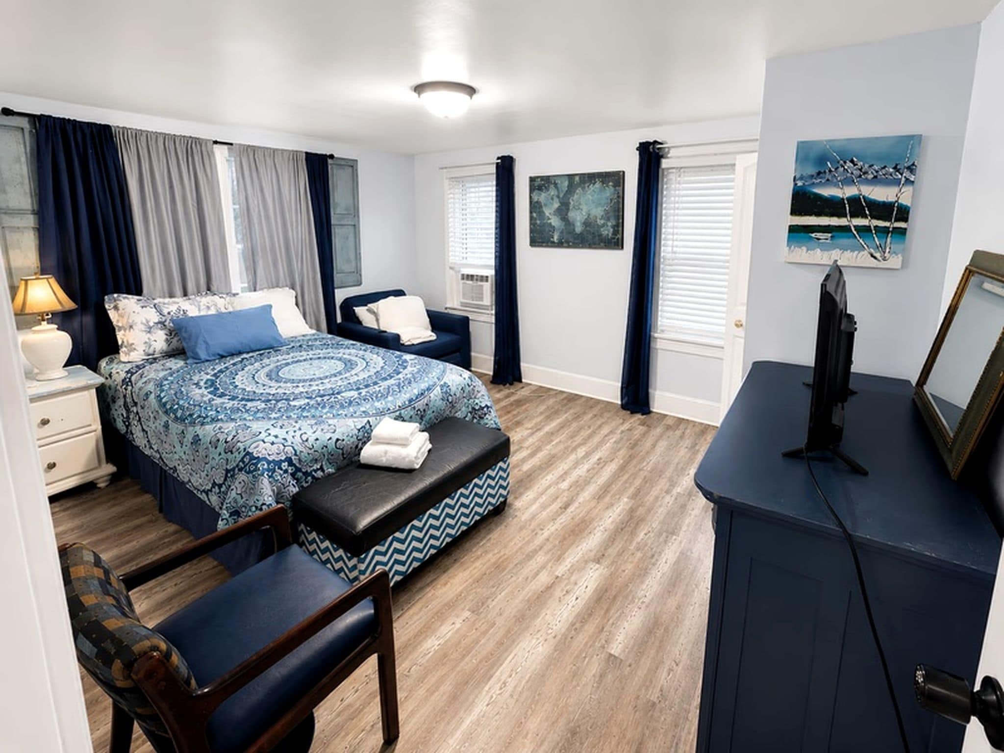 A bedroom with a bed, a desk, a chair, a bench, a TV, and artwork on the walls.