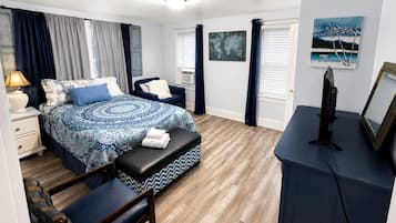 A bedroom with a bed, a desk, a chair, a bench, a TV, and artwork on the walls.