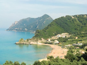 Eine Küstenlandschaft mit Strand, Felsen und Bergen im Hintergrund.