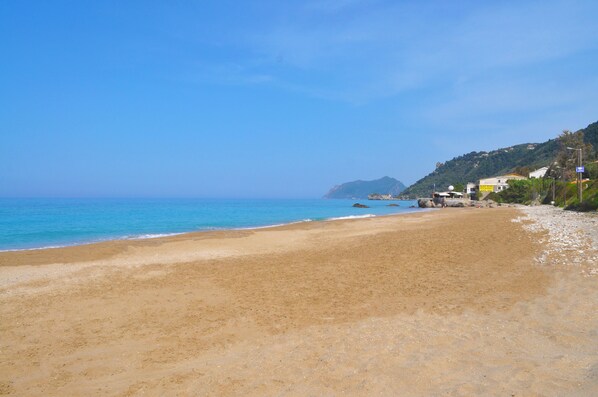 A beach with a clear view of the ocean and a hilly landscape in the background.