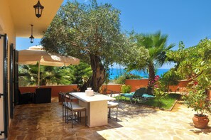Une terrasse avec une table et des chaises, un grand arbre et une vue sur la mer.