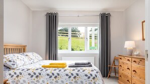 Une chambre à coucher avec un lit, une commode, une fenêtre avec des rideaux et une vue sur l’extérieur.