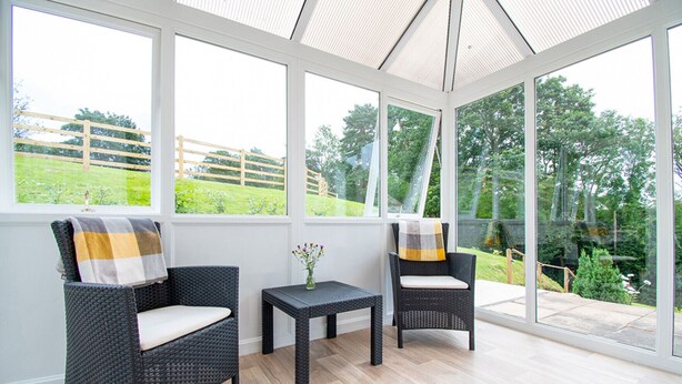 Une véranda meublée de mobilier en osier, avec une petite table et un vase de fleurs.