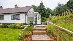 Une maison avec un jardin, des marches en bois et une véranda en verre.