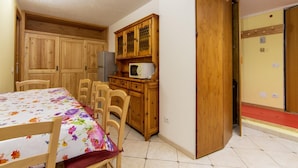 A dining area with a table set for four, wooden cabinets, a microwave, and a door leading to another room. - Residence Cervinia 3952 (Valtournenche)