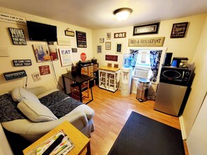 A compact living space with a sofa, a small dining table, a kitchenette, and various motivational wall decorations. - Room-cozy Yellow Queen Bed By Yale U (New Haven)