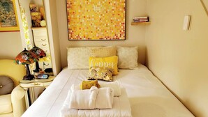 Cama bem arrumada com almofadas, mesa de cabeceira com abajur e parede com arte em mosaico.