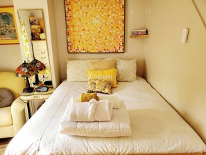 Cama bem arrumada com almofadas, mesa de cabeceira com abajur e parede com arte em mosaico.