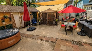 A backyard patio with a Coleman inflatable hot tub, a covered seating area, and a red umbrella.