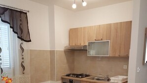 A compact kitchen with wooden cabinets, a gas stove, a microwave, and a sink. There is a dining table with chairs and a vase of flowers. - Apartments Božić (Novi Vinodolski)