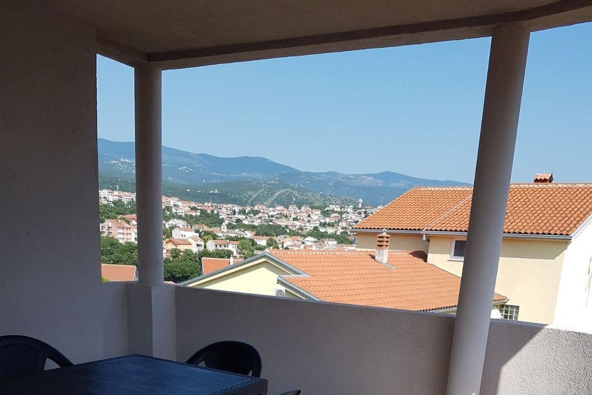 A covered outdoor area with a table and chairs, a view of a town and mountains in the distance.