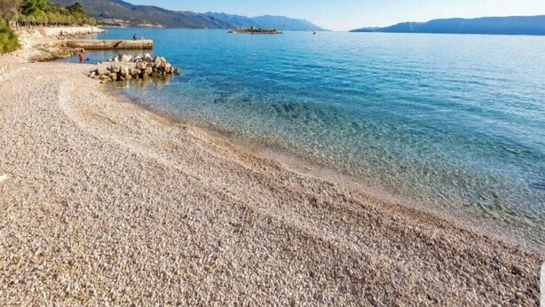 A pebble beach with clear water, a rocky outcrop, and distant mountains. - Apartments Božić (Novi Vinodolski)