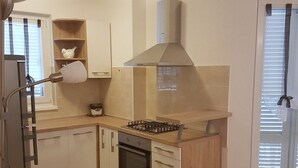 A compact kitchen with a gas stove, oven, and a modern range hood. - Apartments Božić (Novi Vinodolski)