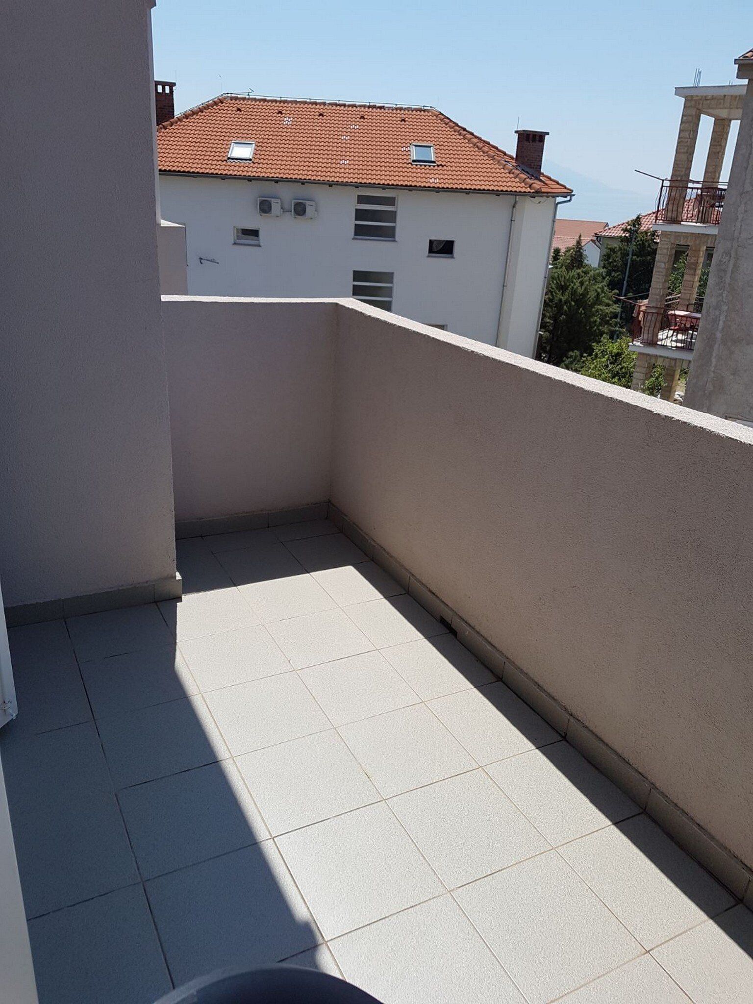 A small, enclosed balcony with tiled flooring and a view of a building with a tiled roof.