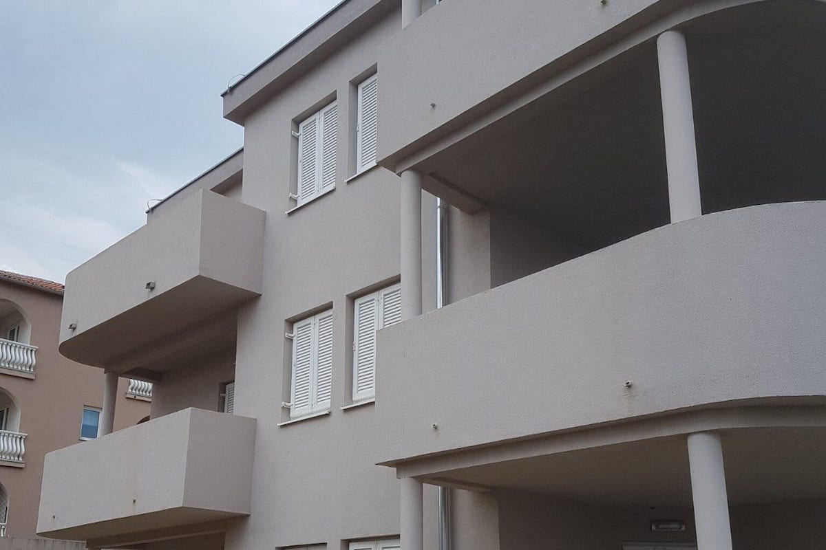 A multi-story residential building with balconies, a covered outdoor seating area, and a visible door.