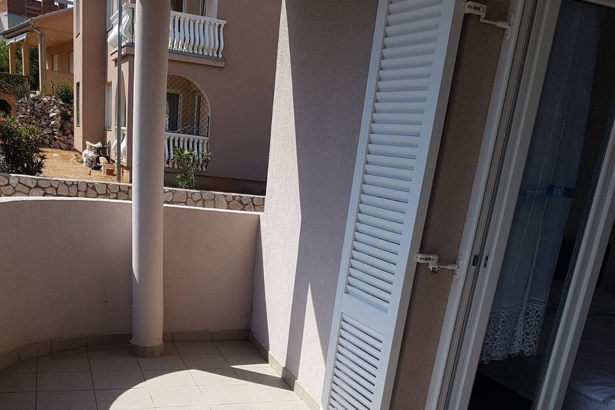 A balcony with white shutters, a tiled floor, and a view of a building with a balcony.