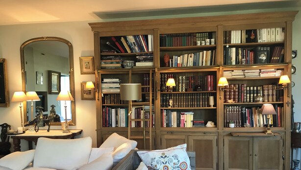 Ein gemütliches Wohnzimmer mit einer großen Bücherwand voller Bücher, einem bequemen Sofa mit weißen Kissen und einem Holztisch.