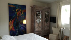 Ein Hotelzimmer mit einem großen Bett, einem hölzernen Schrank, einem Schreibtisch mit Stuhl, einem Fernseher und einem farbenfrohen abstrakten Gemälde an der Wand.