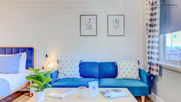 Un salon moderne avec un canapé bleu, une table basse en bois et une plante en pot. Des illustrations botaniques encadrées ornent le mur.