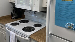 Een keuken met witte kasten, een magnetron, een fornuis en een koelkast. Op de koelkast staat een briefje en op het aanrecht staat een koffiezetapparaat.