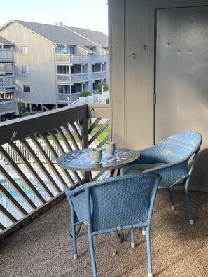 En balkon med to fletstole og et lille bord, der kigger ud over et boligområde med høje bygninger.